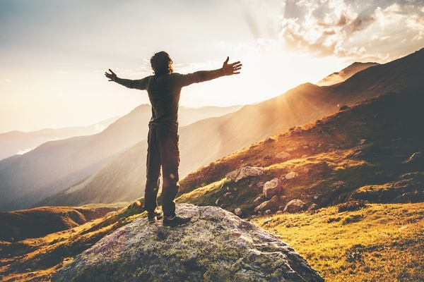 Man standing on a rock with his arms spread wide as the sun rises.